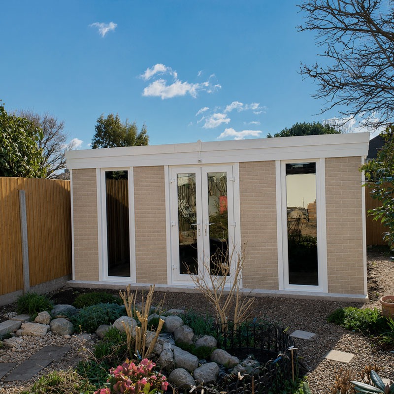 GARDEN-BRICK-2 - All Seasons Steel Buildings Small beige brick garden room with white-framed glass doors in a fenced backyard with a rock garden and plants.