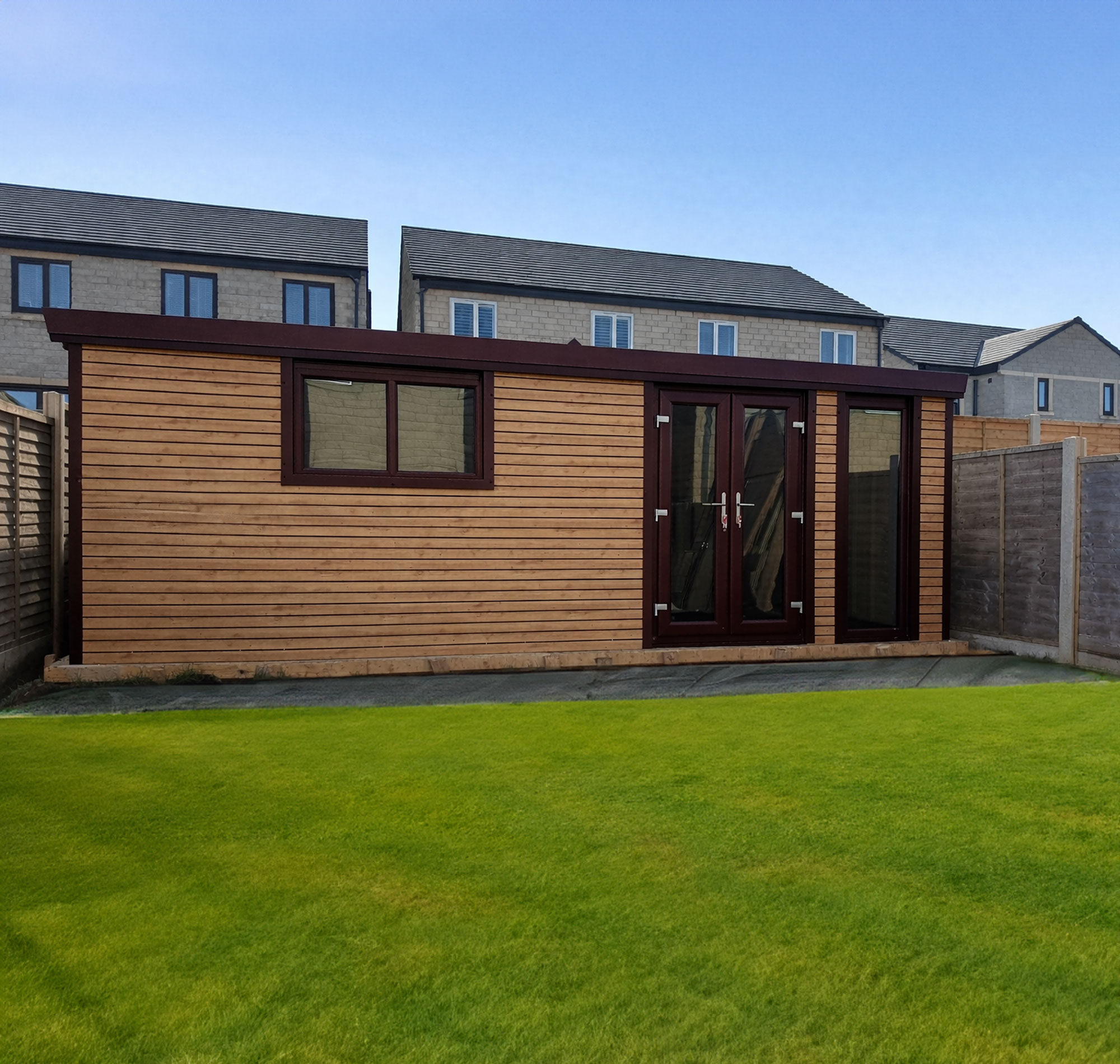 MAIN-WOOD-GARDEN - All Seasons Steel Buildings Wooden garden shed in a backyard with a green lawn and brick houses against a clear blue sky.