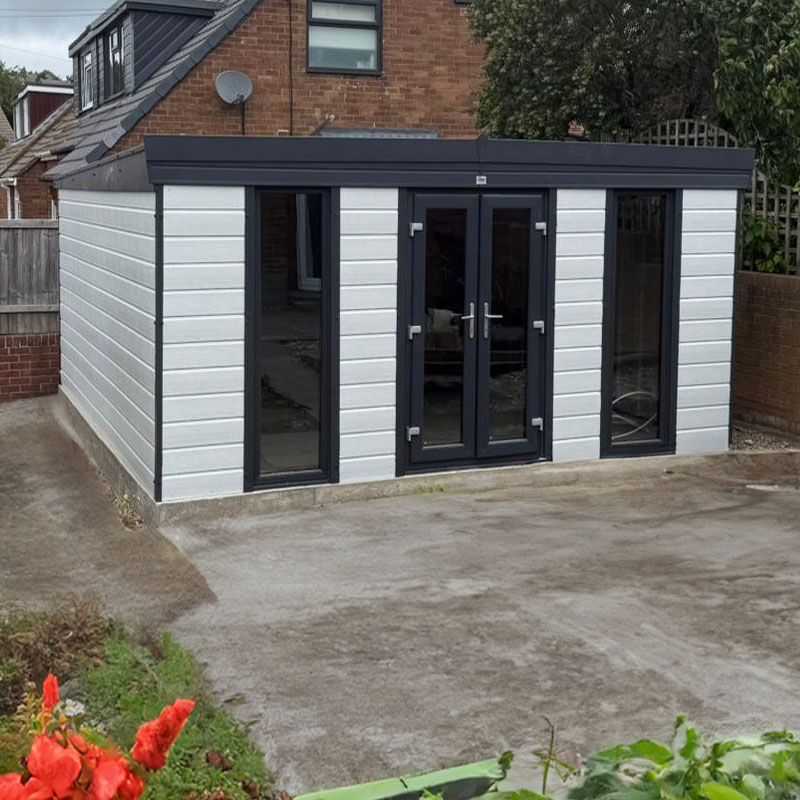 Grey-framed garden room/conservatory with double doors and tall glass panels, in a paved backyard behind a brick house.