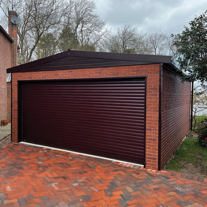 Brick garage with a dark maroon roller door and a pitched roof, next to a red brick driveway.