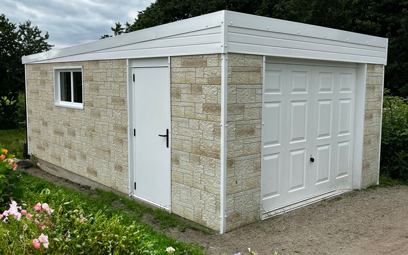 Stone outbuilding with beige brick pattern, white side door, small window, and large white garage door on a dirt path.