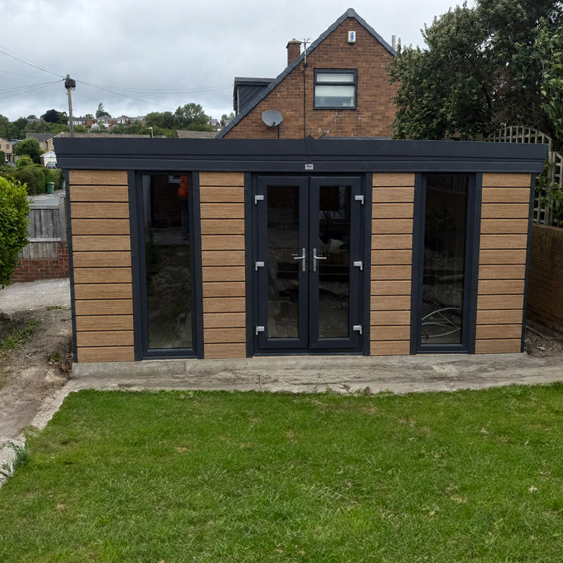 WOOD-GARDEN1 - All Seasons Steel Buildings Garden room or modern shed with dark frame and wooden paneling, glass doors, and large side windows in a backyard setting.