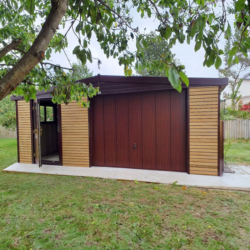 Wooden shed with a large double garage-style door and an open side door, under leafy branches in a grassy backyard by a fence.