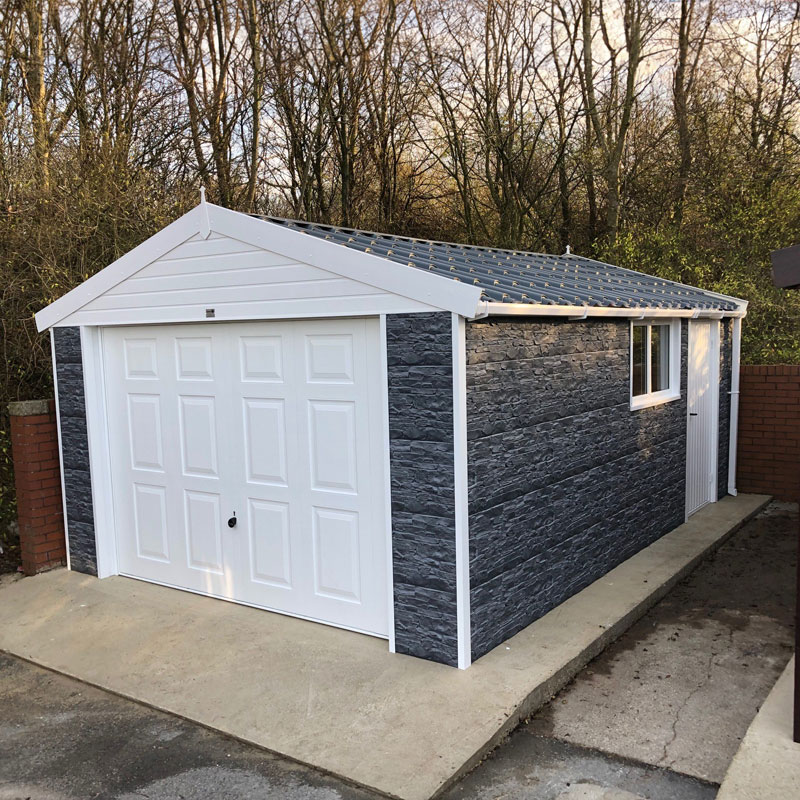 Light blue-gray single-car garage with a white paneled double door and dark slate-like cladding, set on a concrete driveway with a small side door and window under a gabled roof.