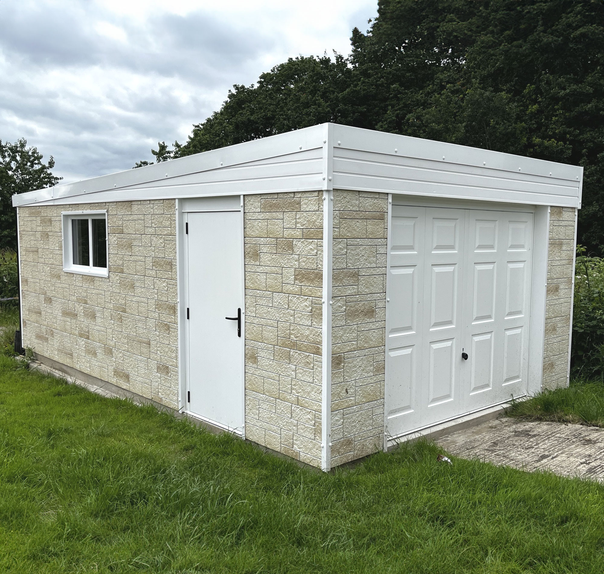 Beige stone outbuilding with white doors and trim, set on a grassy lawn under a cloudy sky with trees in the background.