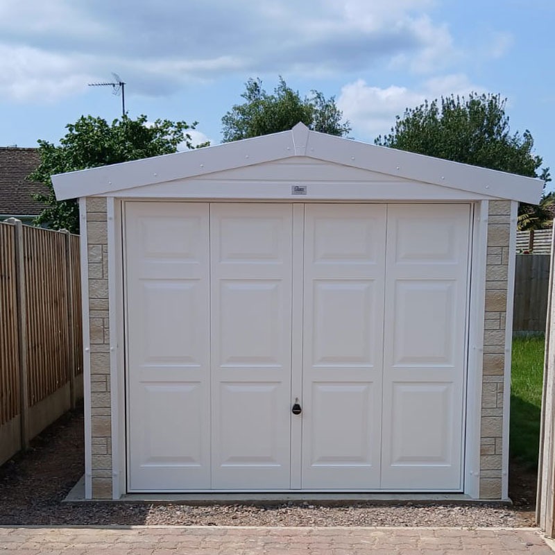 White garden shed with a pitched roof and four-panel double doors in a gravel yard.