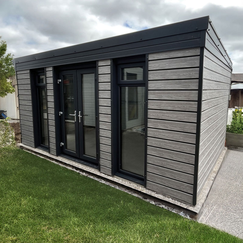 Modern garden shed with black-framed glass doors and grey horizontal wood siding in a lawn setting