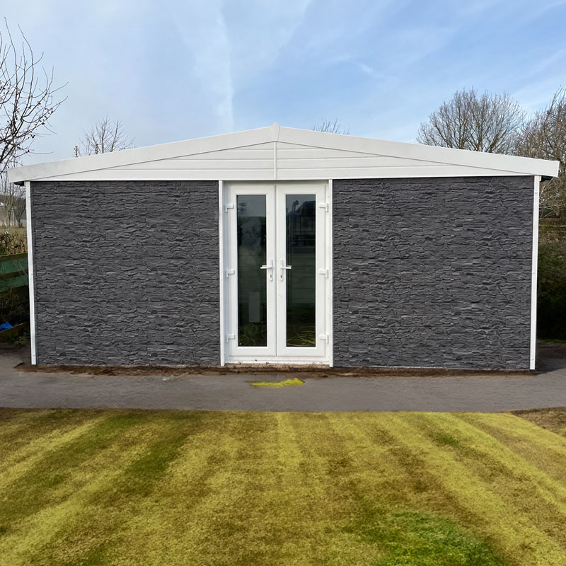 Grey stone shed with a white double door and slanted white roof in a garden yard, daylight scene.