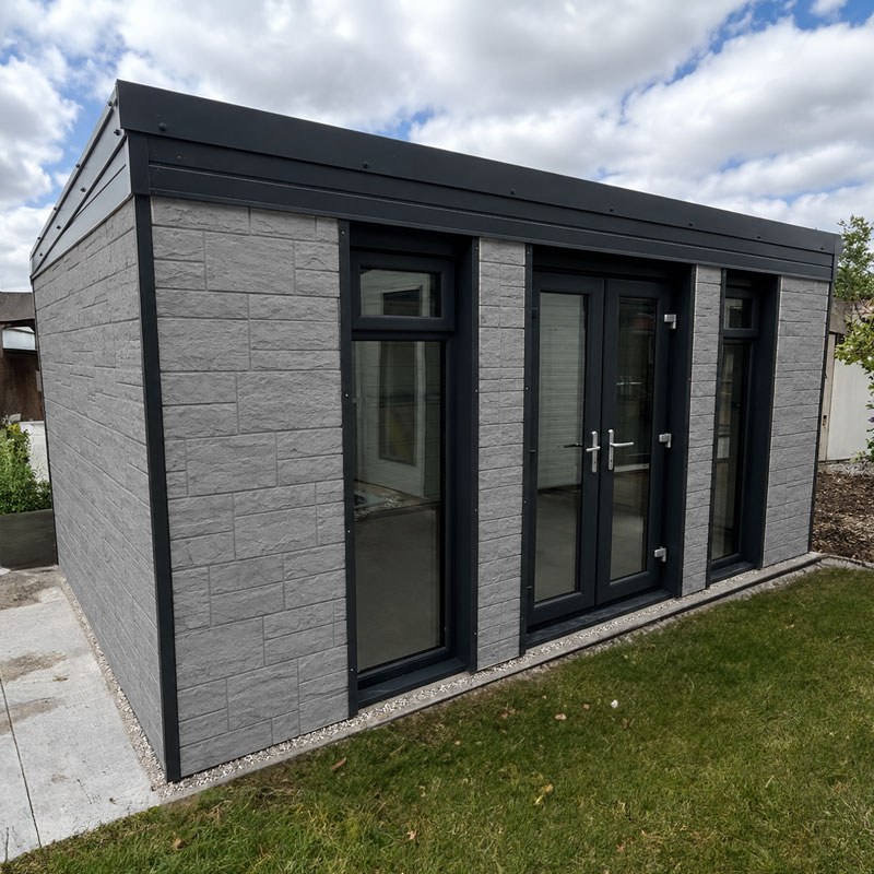 Modern grey brick outbuilding with three tall glass doors and windows, black frames, and a flat roof by a green lawn.