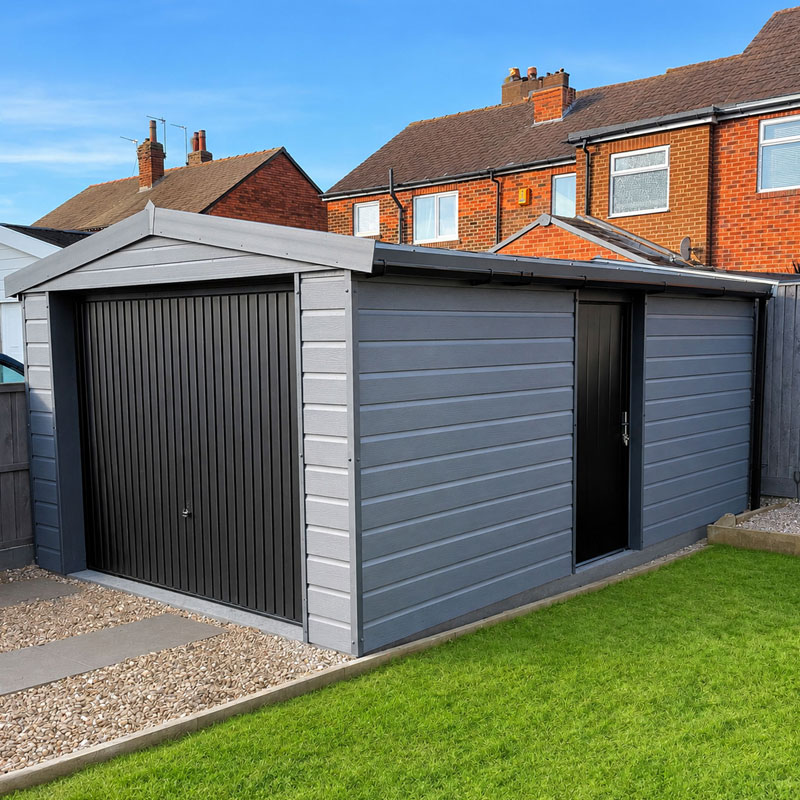 Grey garden shed with a black roller garage door and a black side door in a suburban backyard, with a lawn and gravel path nearby.